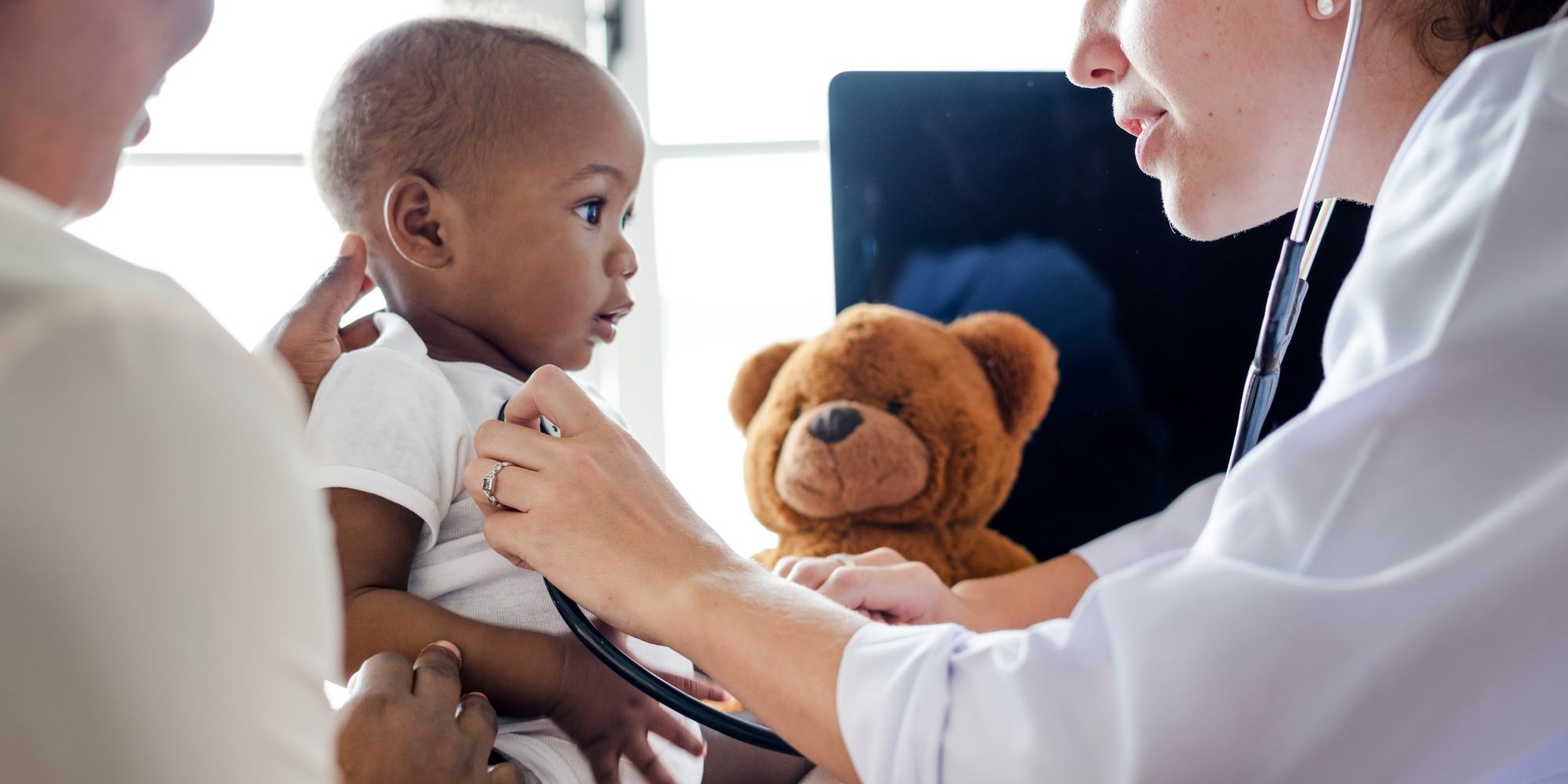 A doctor cares for a small baby with a teddy bear in the background