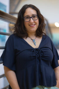 Elizabeth Fernandez, science writer, headshot. She is wearing a blue shirt, glasses, and a blue necklace